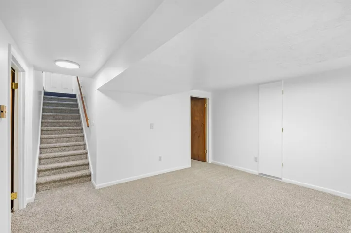 Carpeted flooring extending into a carpeted staircase with a wood handrail, white walls, and a recessed ceiling light