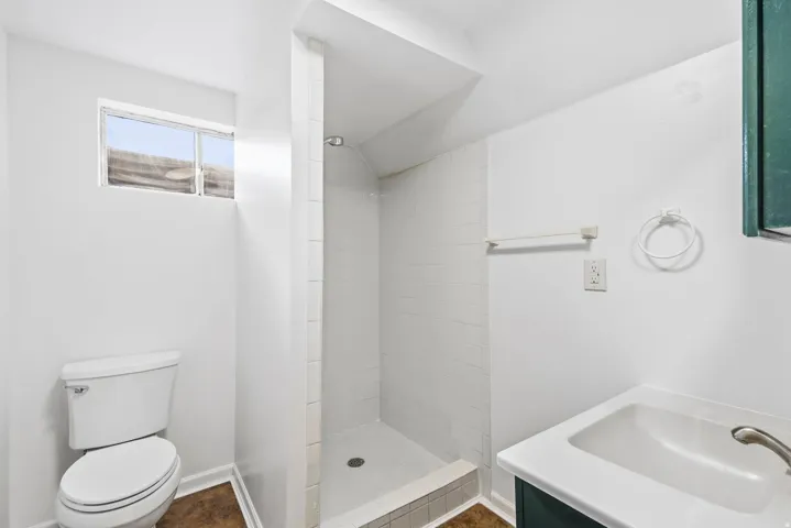 White tiled shower stall with a single showerhead, white toilet, and a vanity with an integrated sink