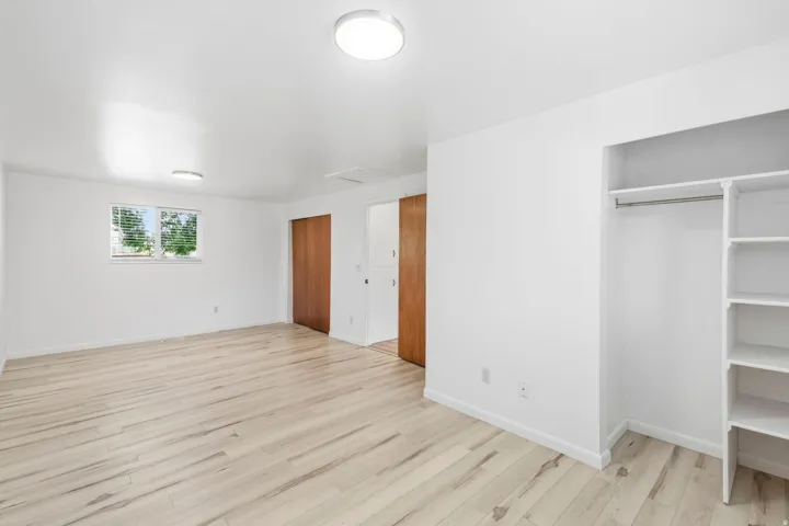 Light wood-finish flooring, white walls, built-in closet shelving, and a horizontal window with blinds