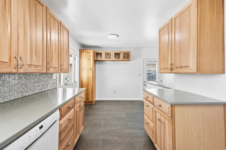 Wood cabinetry, light-toned countertops, and mosaic tile backsplash