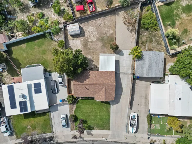 Expansive lot featuring a main residence with a brown shingle roof, a detached structure with a corrugated metal roof, a second detached structure with a white corrugated metal roof, and concrete paving throughout the property