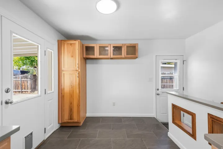 Slate-finish tile flooring, natural wood cabinetry with glass-front uppers, and a peninsula with a composite countertop