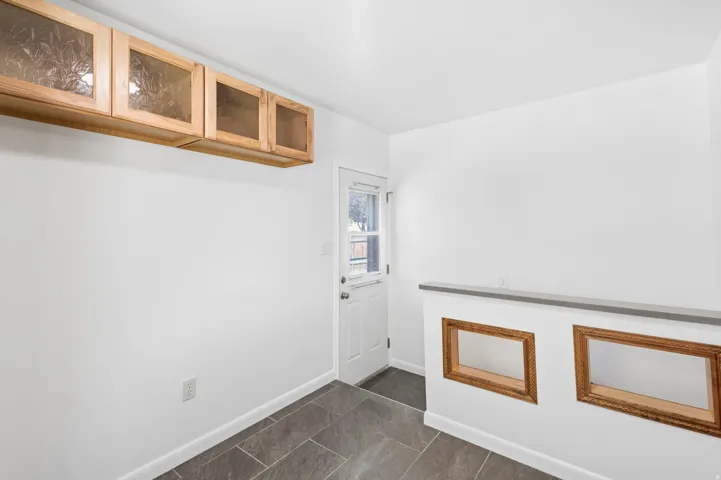 Wood-finish upper cabinets with frosted glass panels, white walls, and dark rectangular floor tiles