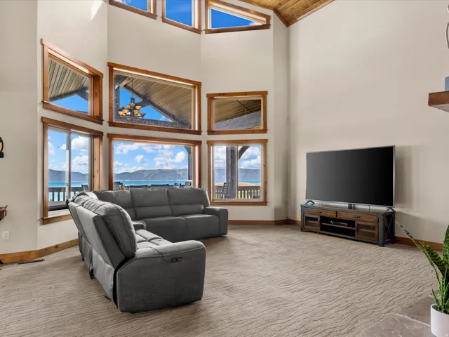 Vaulted ceiling with exposed wood beams, expansive windows with wood trim, light-colored walls, carpet flooring, and a sliding glass door