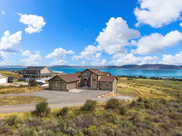 Contemporary-style residence with a stone and siding exterior, multiple garages, and a paved driveway, set against a prominent lake and distant mountains