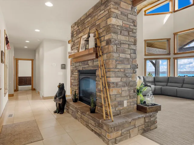 Floor-to-ceiling stone fireplace with a wood mantle, vaulted ceilings, recessed lighting, and large windows with wood-trim framing