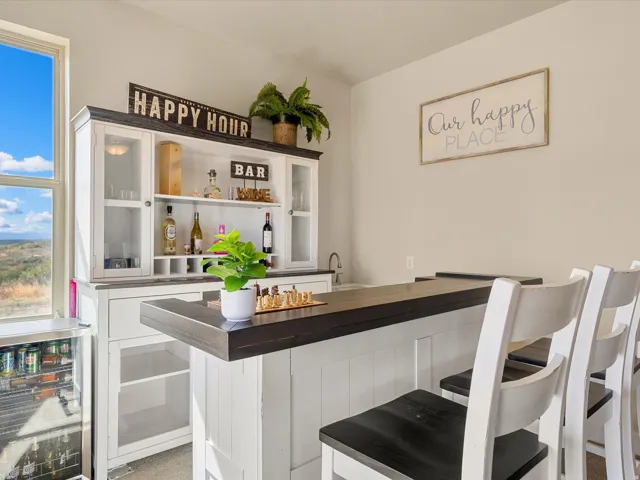 Built-in bar with dark countertop, white cabinetry with glass-front uppers, and an integrated sink