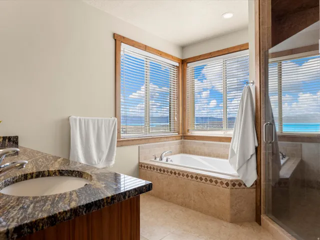 Built-in soaking tub with decorative tile surround, walk-in shower with glass enclosure, vanity with integrated sink and stone countertop, and tile flooring