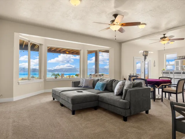Expansive windows showcasing distant water scenery, multiple ceiling fans, recessed lighting, and carpeted flooring