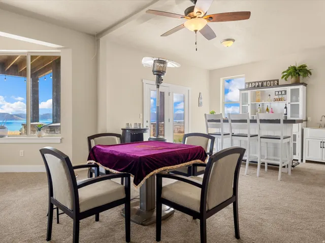 Built-in wet bar with white cabinetry and a sink, broad windows, a ceiling fan, and access to an outdoor area