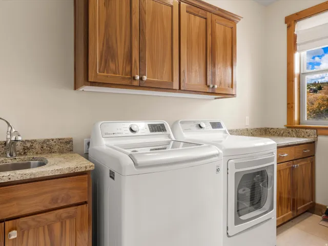 Upper and lower cabinetry with wood finishes, stone-finish countertops, and a stainless steel sink with a gooseneck faucet