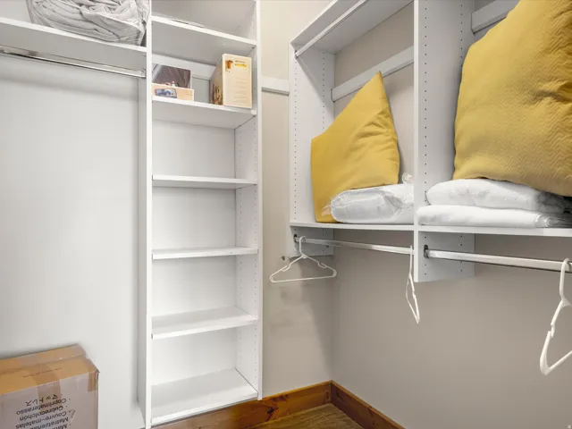 White shelving units providing organized storage, multiple hanging rods, and wood-finish flooring