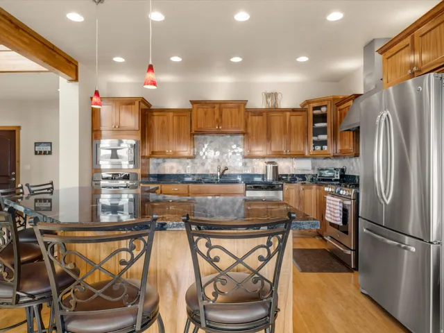 Kitchen featuring wood cabinetry, stainless steel appliances, dark stone countertops, a tiled backsplash, and wood-finish flooring