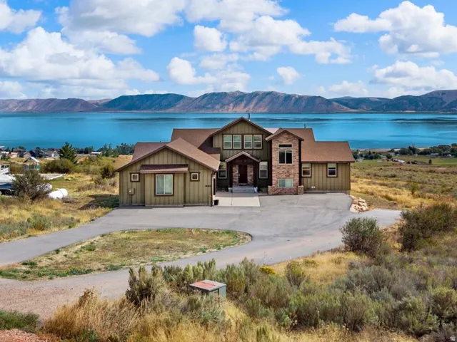 Wood-sided residence featuring a stone-clad entry, attached two-car garage, and a paved driveway