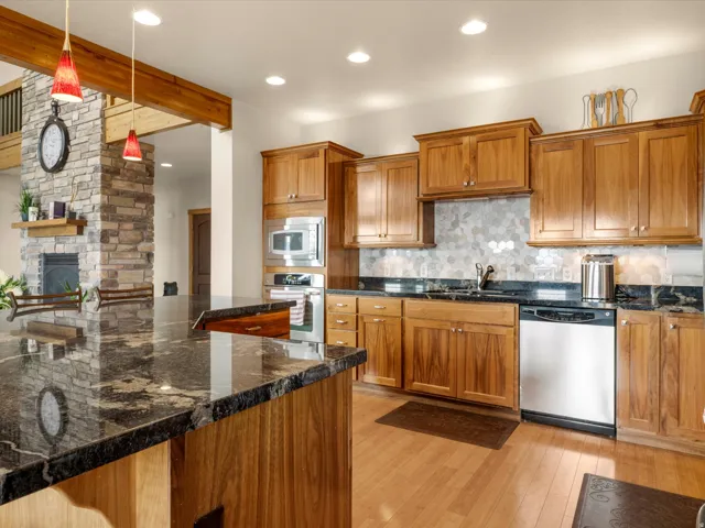 Kitchen featuring wood cabinetry, dark stone countertops, stainless steel appliances, and a tile backsplash