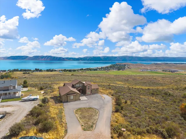 Expansive property with a large driveway, a multi-level residence with a brown roof, and a distant body of water