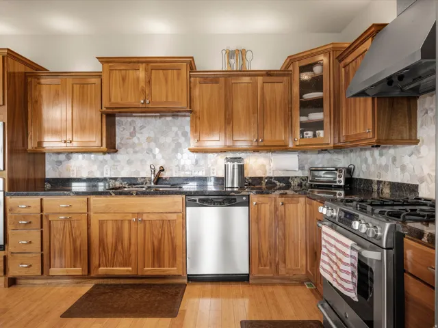 Warm wood cabinetry with crown molding, solid surface countertops, a tile backsplash, and stainless steel appliances