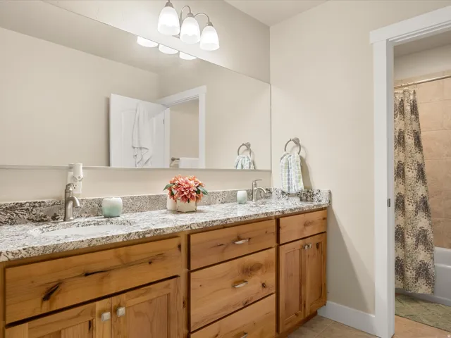 Dual vanity with light-tone wood cabinetry, speckled countertop, and under-mount sinks