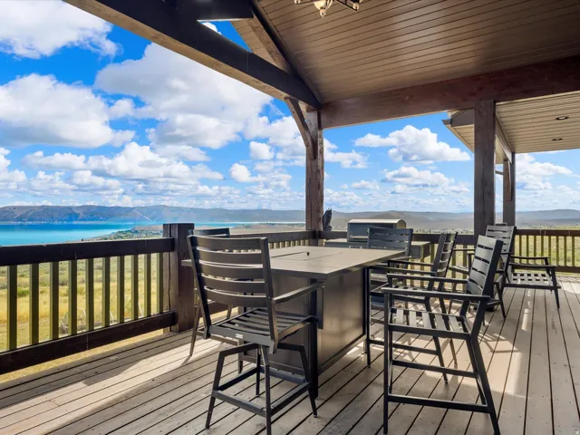 Expansive covered deck featuring a wood-plank floor, exposed wood beams, and a wood railing with lake view