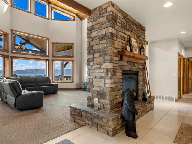 Stone fireplace with a wood-mantel, vaulted ceilings with exposed wood beams, and large windows with wood trim