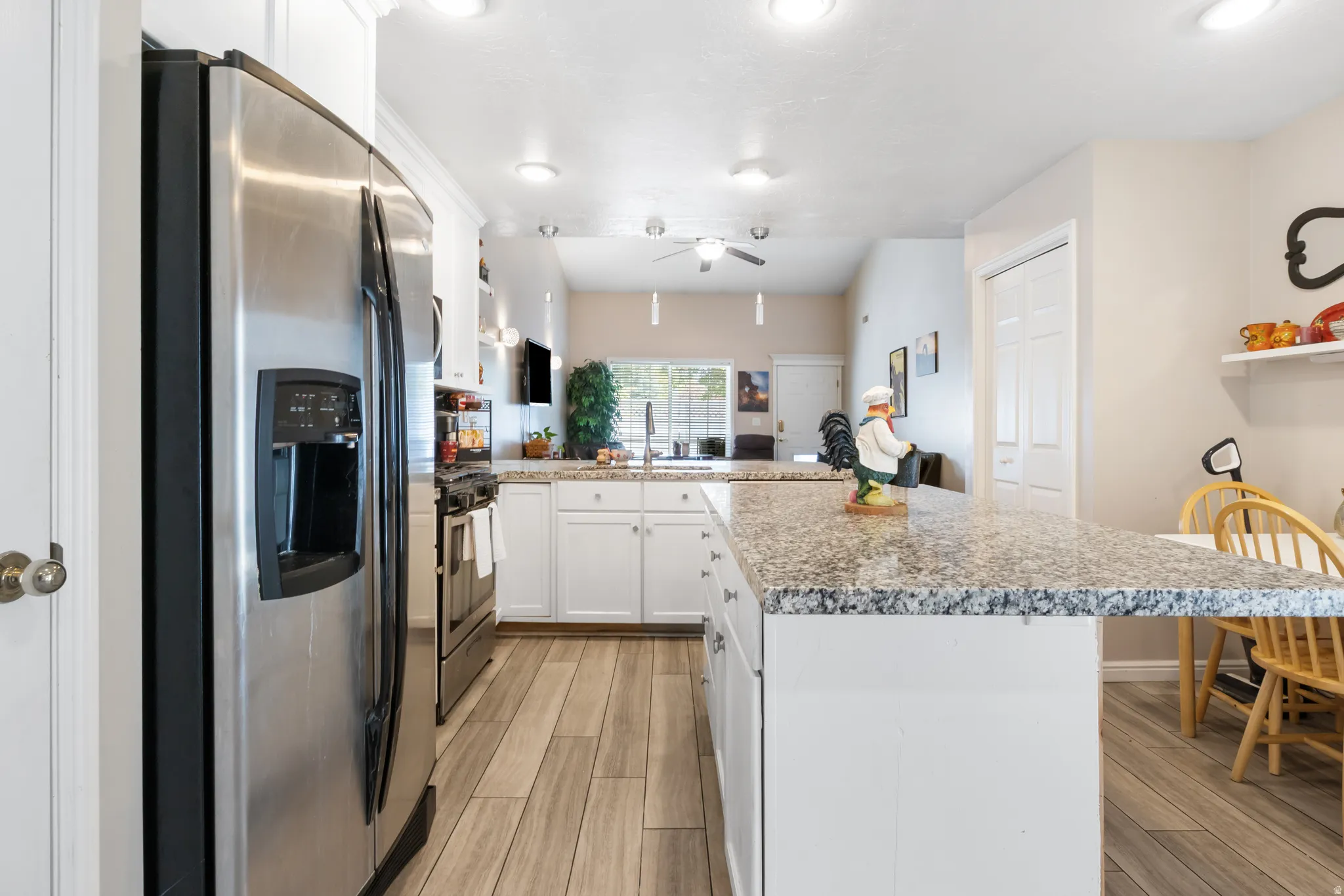 Stainless steel refrigerator, white cabinetry, granite countertops, wood-finish flooring, and recessed lighting