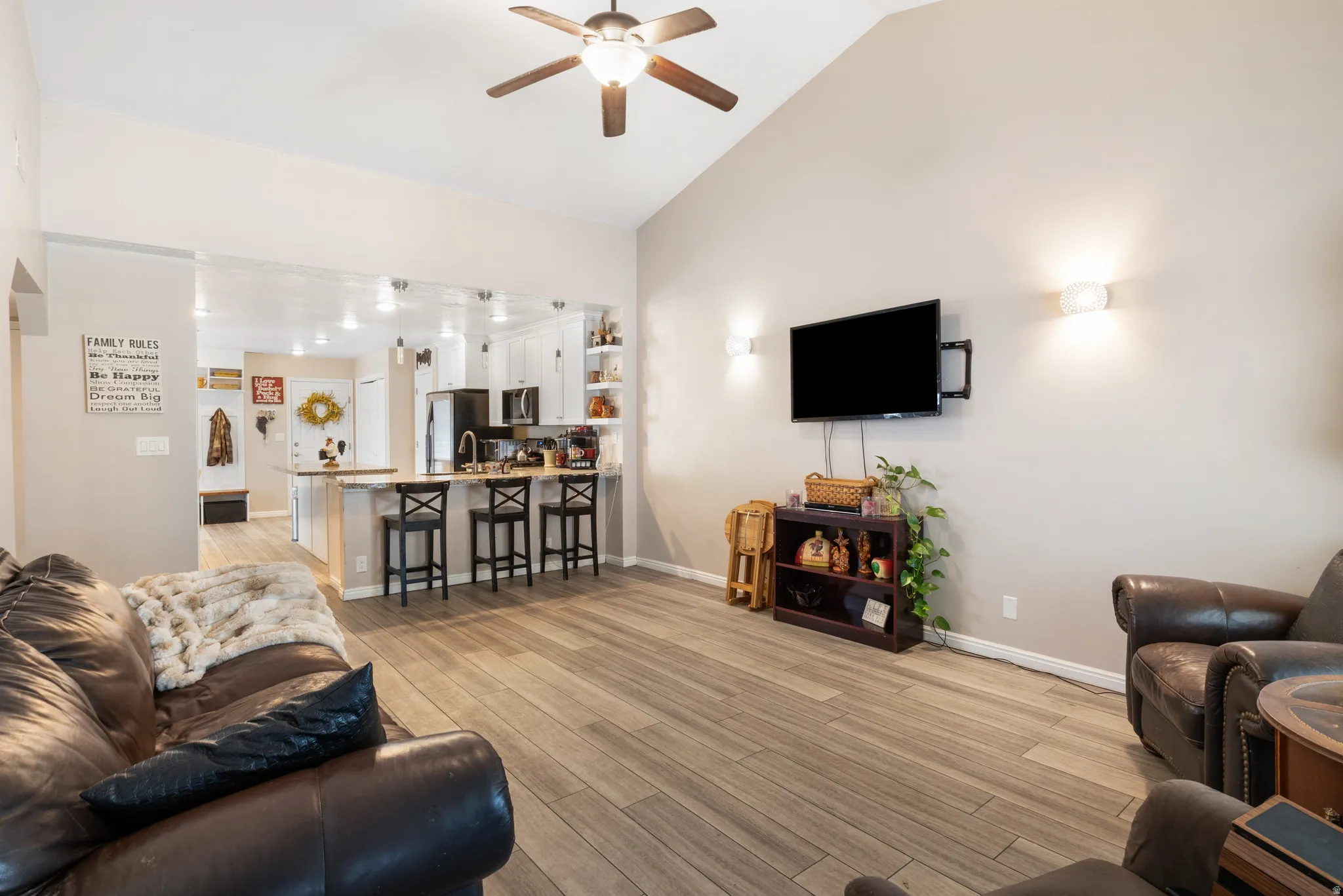 Vaulted ceiling with a ceiling fan, wood-finish flooring, recessed lighting, and a kitchen island with seating
