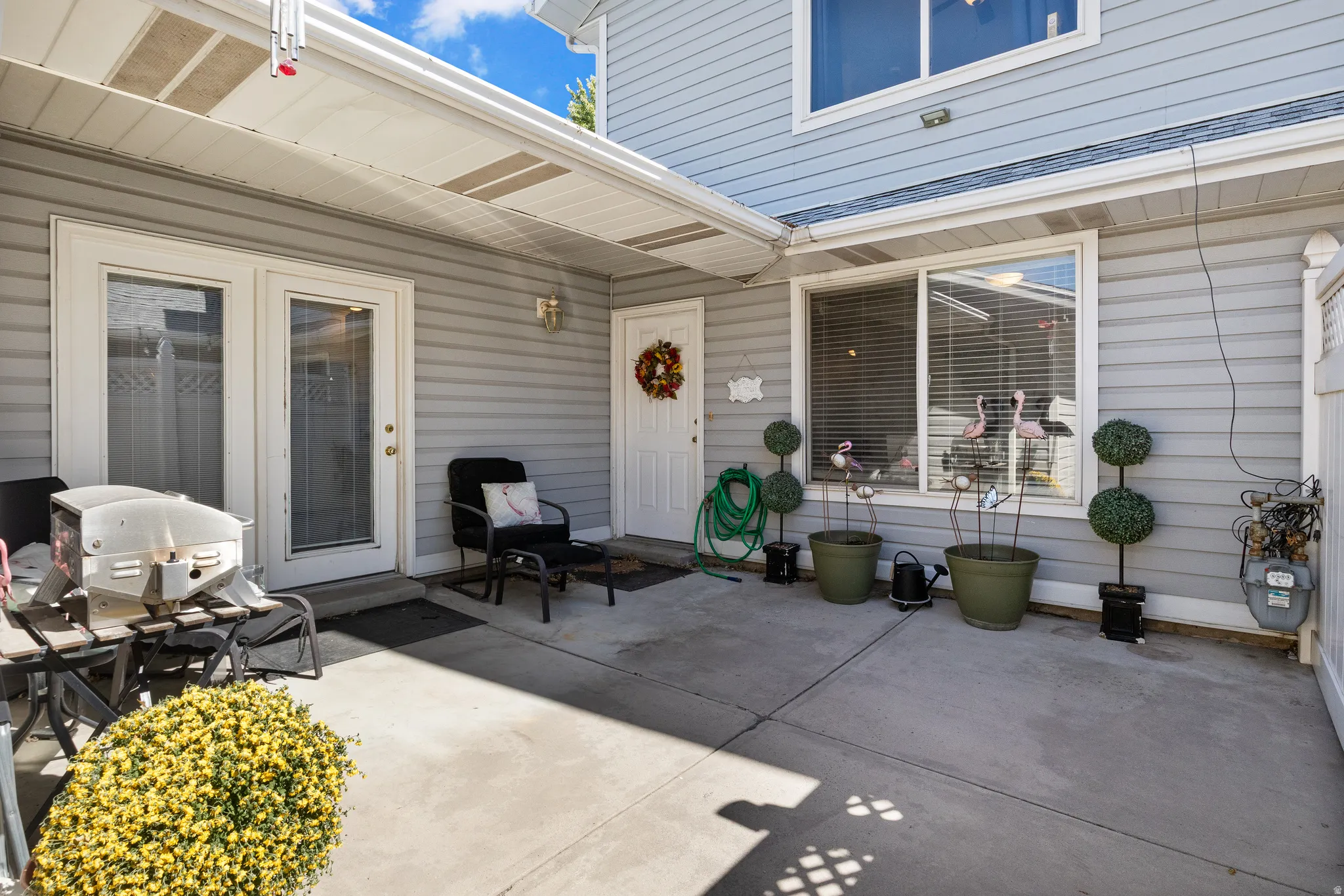 Covered concrete patio with light gray siding, dual French doors, and an additional white entry door