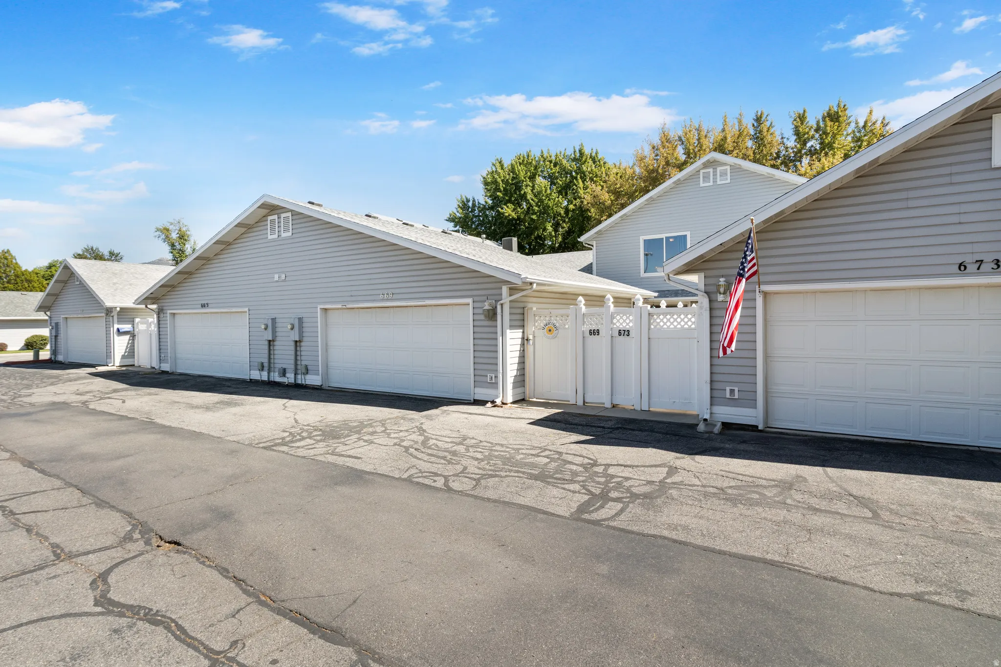 Siding exterior, multiple attached garages with overhead doors, white privacy fencing, and a separate pedestrian gate