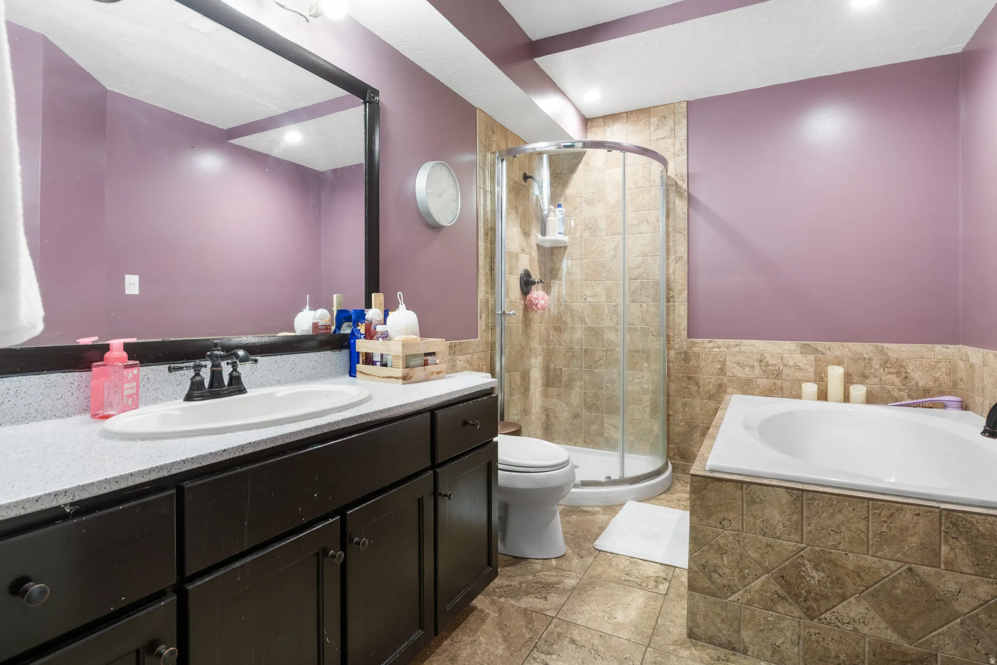 Vanity with a basin sink, large wall-mounted mirror, corner shower with glass enclosure, built-in bathtub, and tiled walls