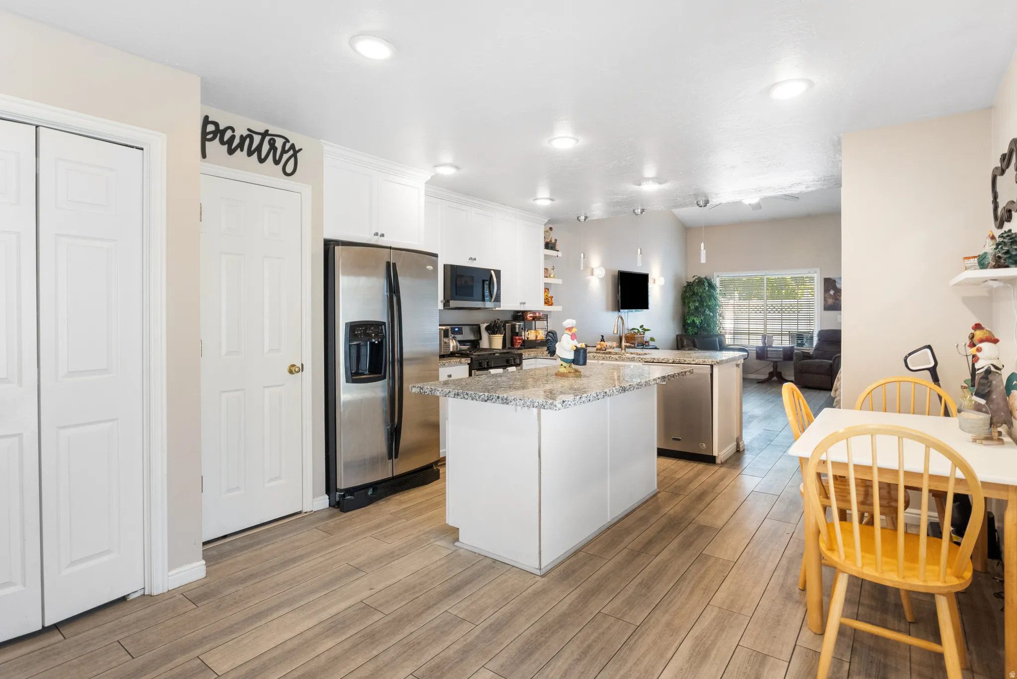 Kitchen featuring wood-finish flooring, white cabinetry, a kitchen island with a granite countertop, and stainless steel appliances
