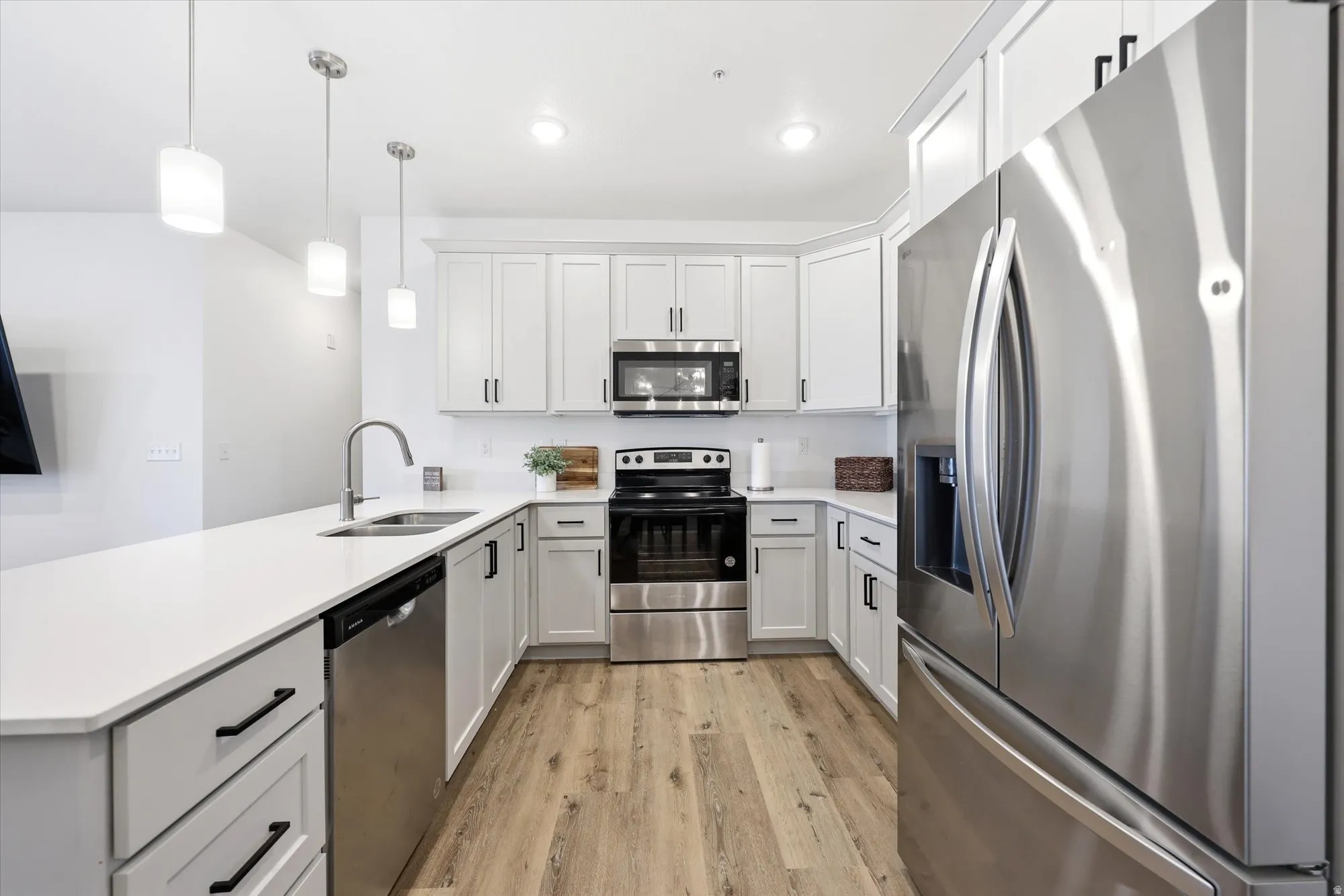 Contemporary kitchen featuring light wood-finish flooring, white cabinetry with black hardware, stainless steel appliances, and a solid surface countertop with an undermount sink