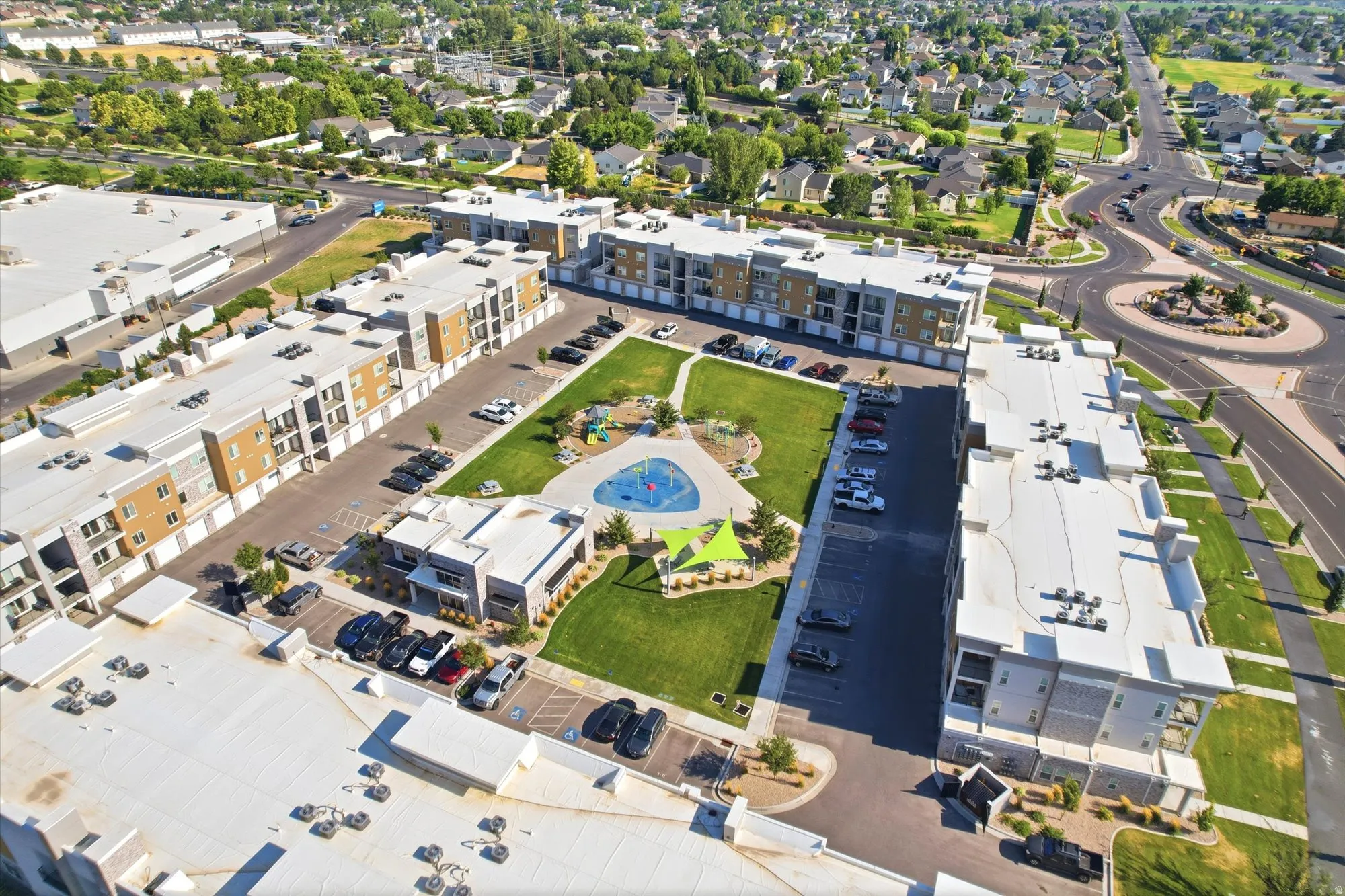 Modern multi-story buildings with balconies, integrated covered parking, manicured green spaces, and a circular road feature