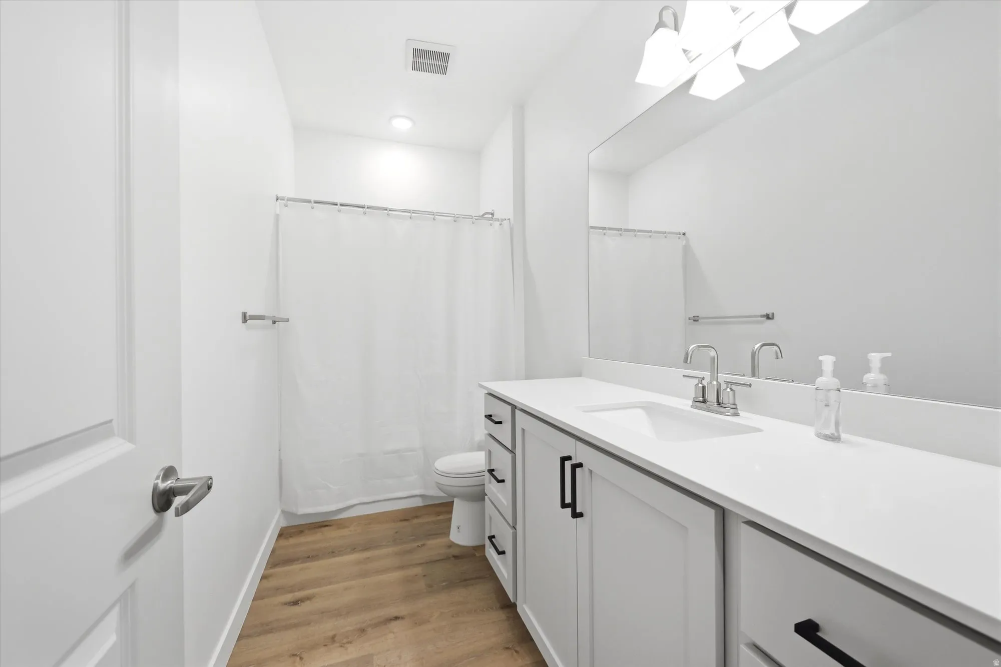 Spacious bathroom featuring a white vanity with integrated sink, chrome faucet, and expansive wall mirror