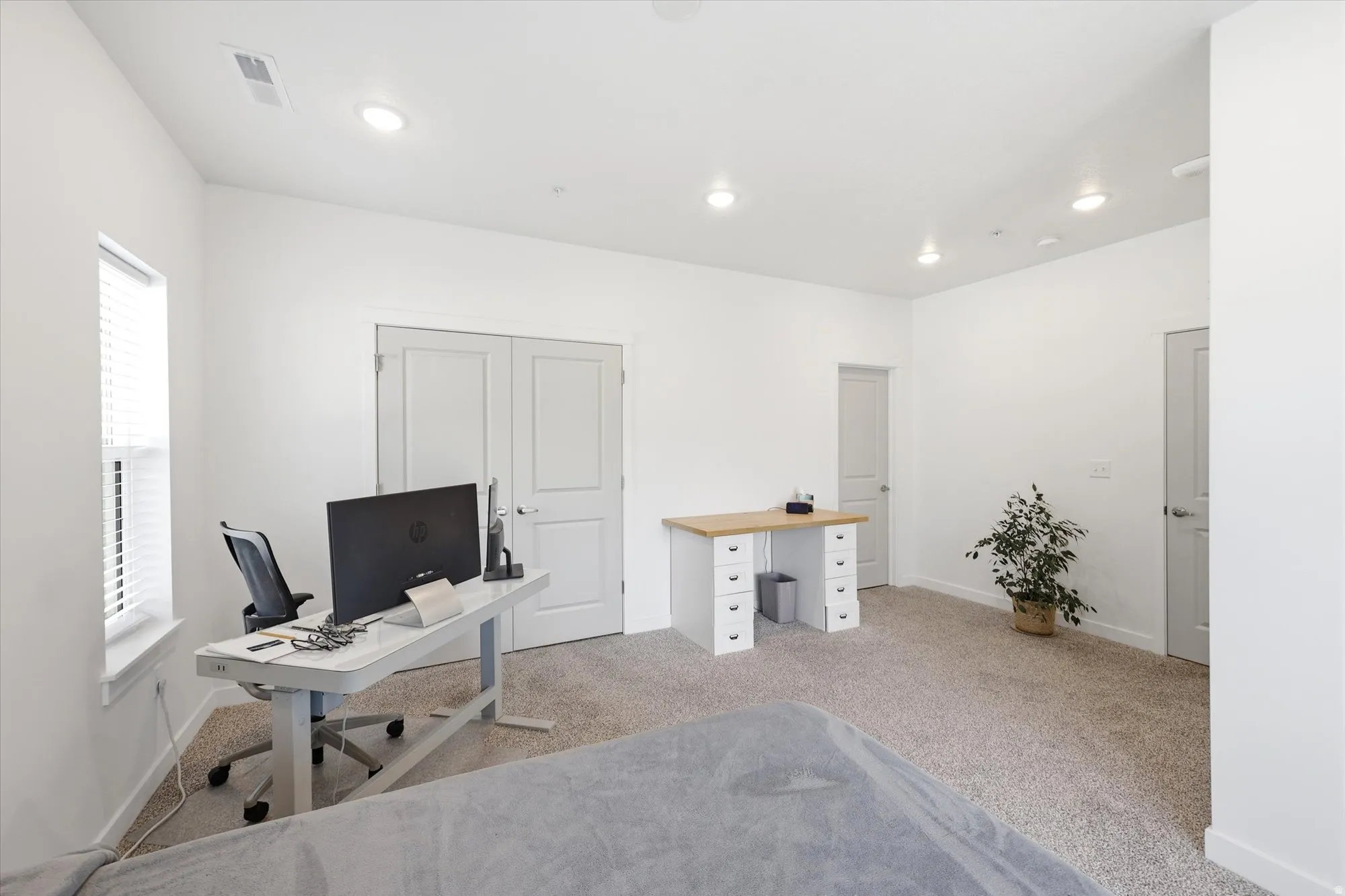 Recessed lighting illuminates a spacious room featuring a window with blinds, carpet flooring, and a pair of double closet doors