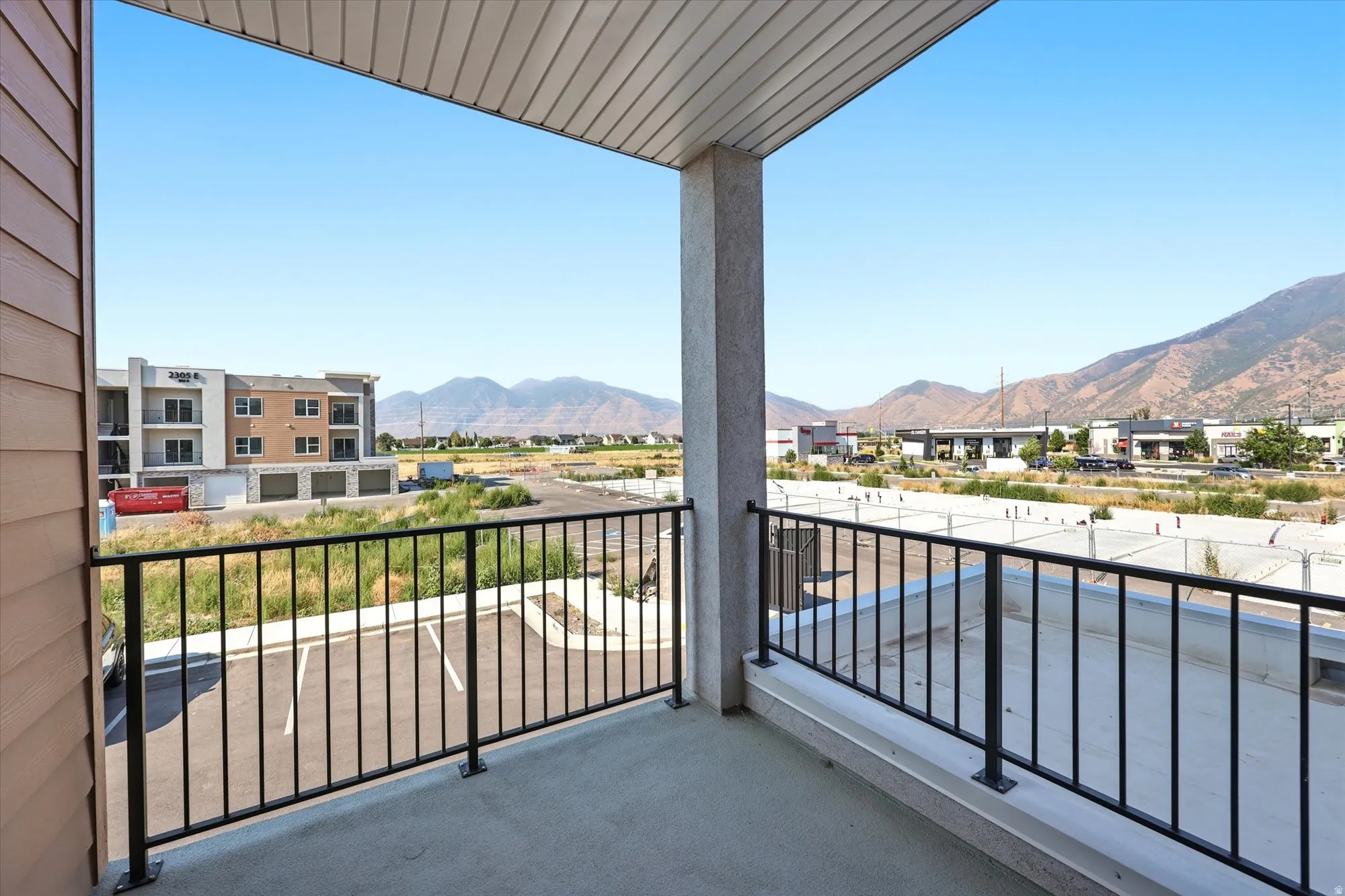 Outdoor balcony with concrete flooring, black metal railing, and a slatted ceiling