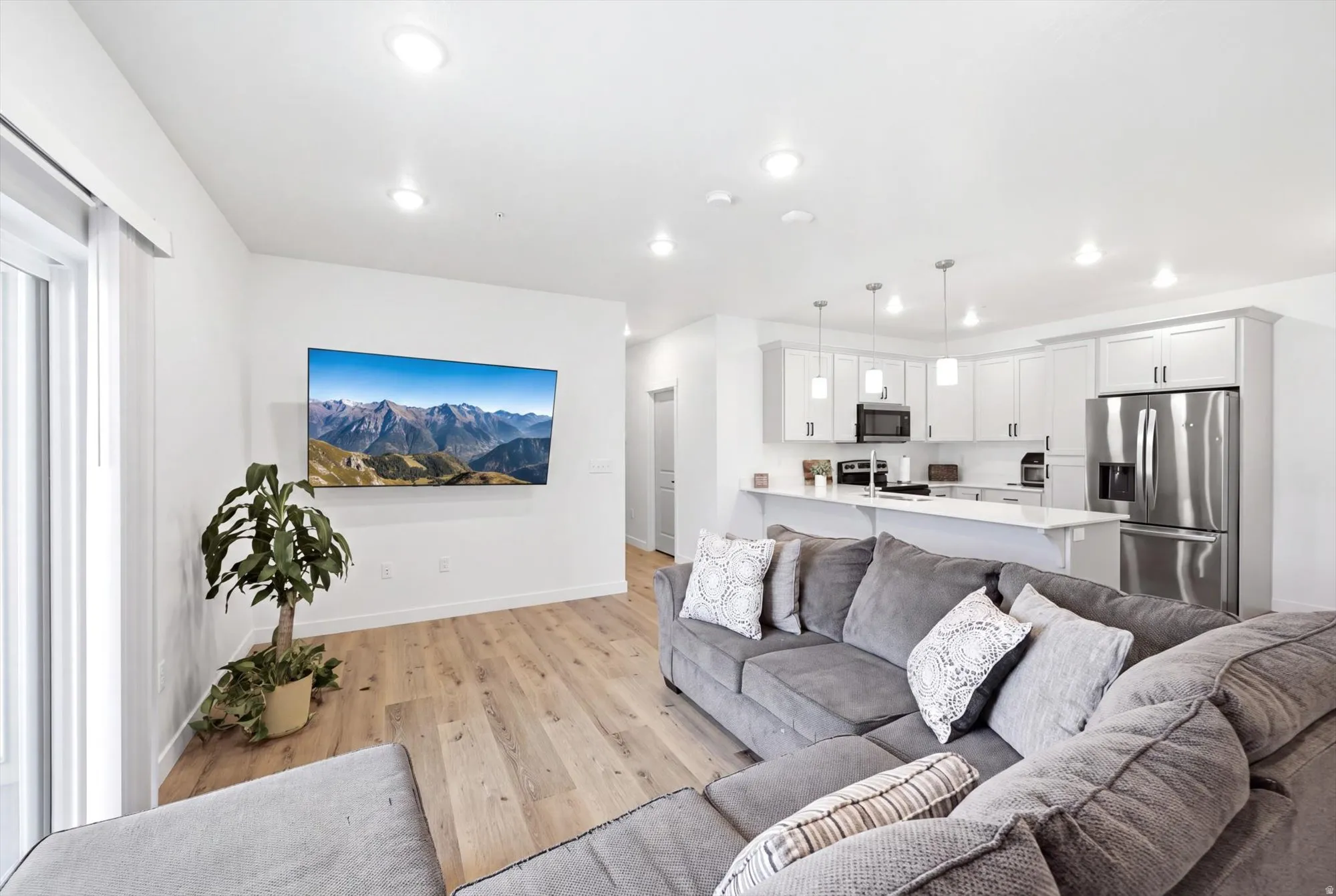 Open-concept living area with wood-finish flooring, recessed lighting, white cabinetry, stainless steel appliances, and a kitchen island with pendant lighting