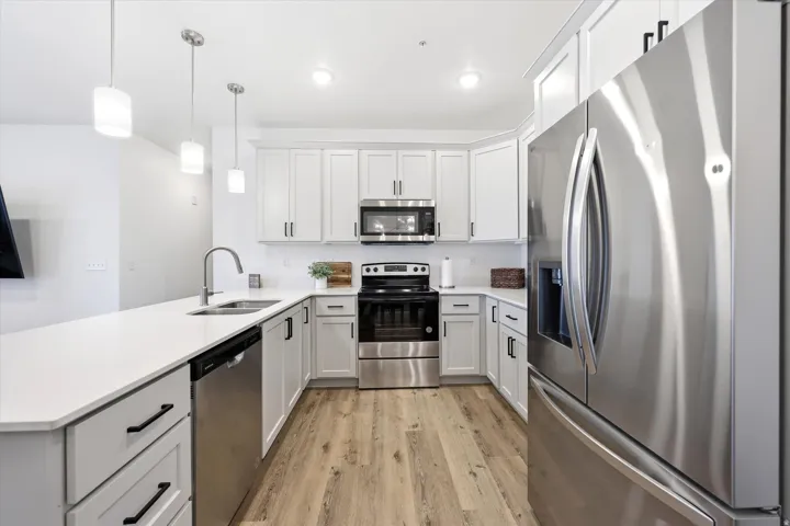 Contemporary kitchen featuring light wood-finish flooring, white cabinetry with black hardware, stainless steel appliances, and a solid surface countertop with an undermount sink