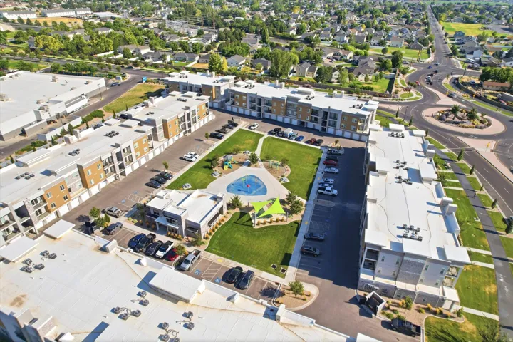 Modern multi-story buildings with balconies, integrated covered parking, manicured green spaces, and a circular road feature