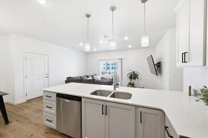Open-concept living space featuring a kitchen island with dual sinks, stainless steel dishwasher, wood-finish flooring, and recessed lighting