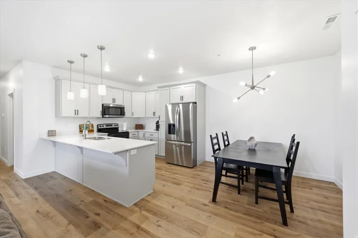 White kitchen cabinetry with black hardware, stainless steel appliances, a white island with pendant lighting, and wood-finish flooring