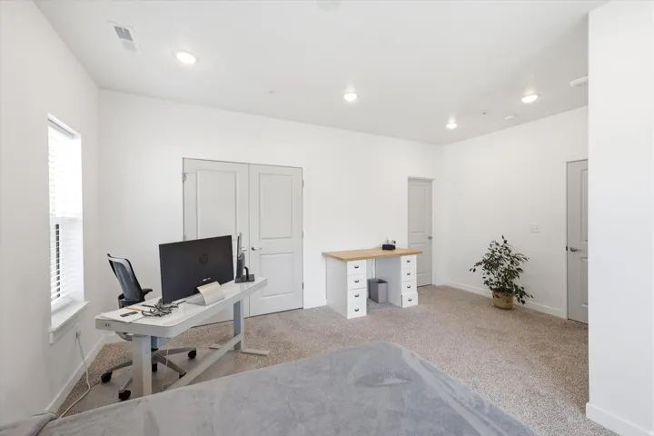 Recessed lighting illuminates a spacious room featuring a window with blinds, carpet flooring, and a pair of double closet doors