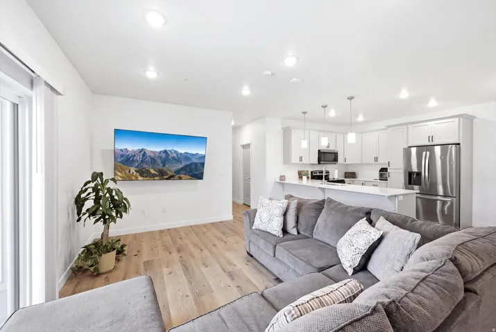 Open-concept living area with wood-finish flooring, recessed lighting, white cabinetry, stainless steel appliances, and a kitchen island with pendant lighting