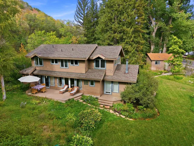 Multi-level residence with a wood-sided exterior, a spacious rear patio, and a separate outbuilding, all set on a landscaped lot with mature trees and a grassy expanse