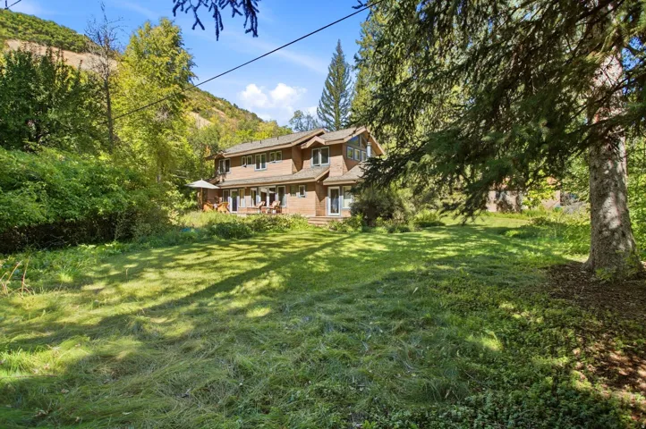 Expansive grassy yard with mature trees and a two-story residence featuring multiple windows and exterior doors