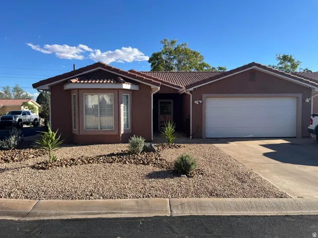 Stucco exterior with a tile roof, featuring a bay window, attached garage, and xeriscaped front yard with decorative rocks