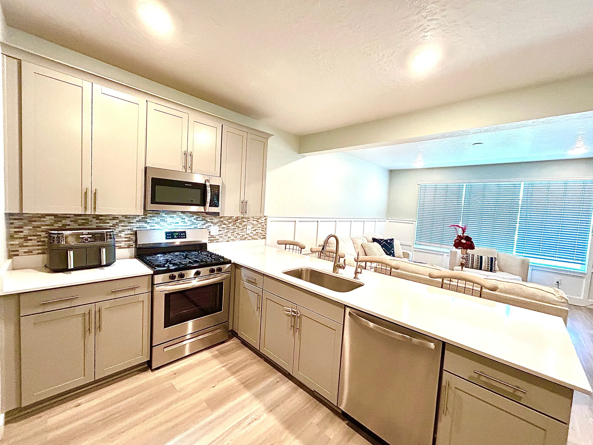 Stainless steel appliances, light-toned cabinetry, mosaic tile backsplash, wood-finish flooring, and white countertops