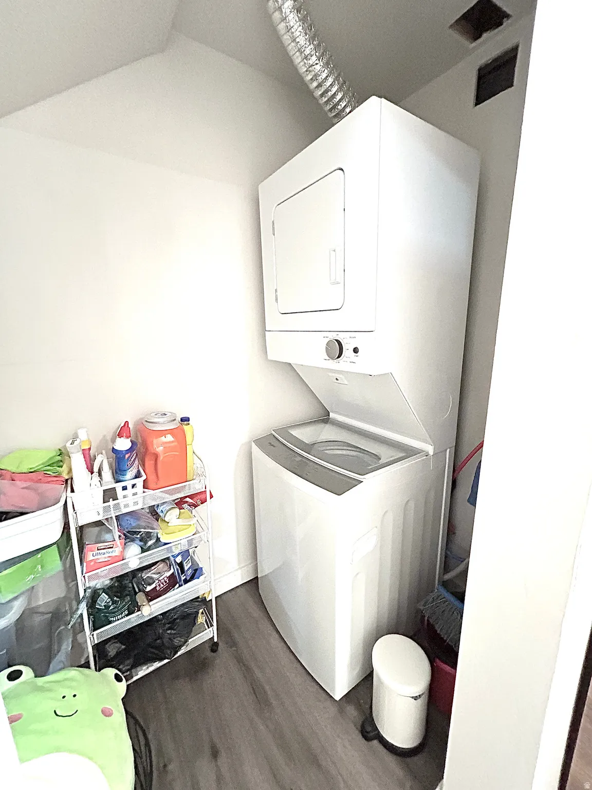Stacked white washer and dryer, wood-finish flooring