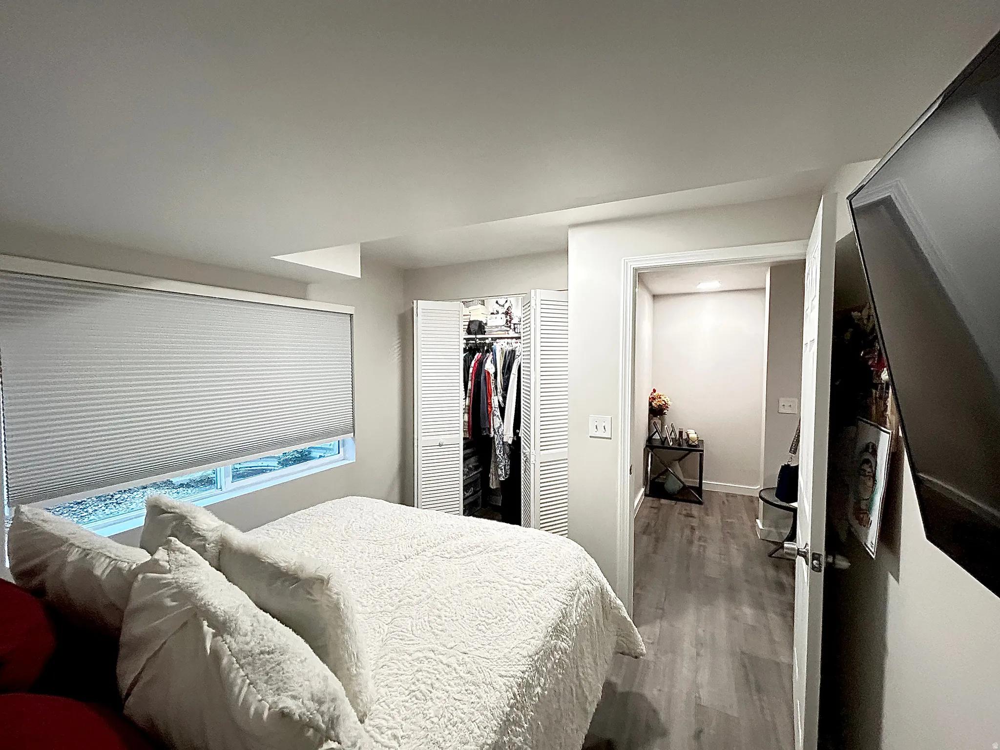 Recessed window with privacy blinds, bi-fold closet doors, and wood-finish flooring