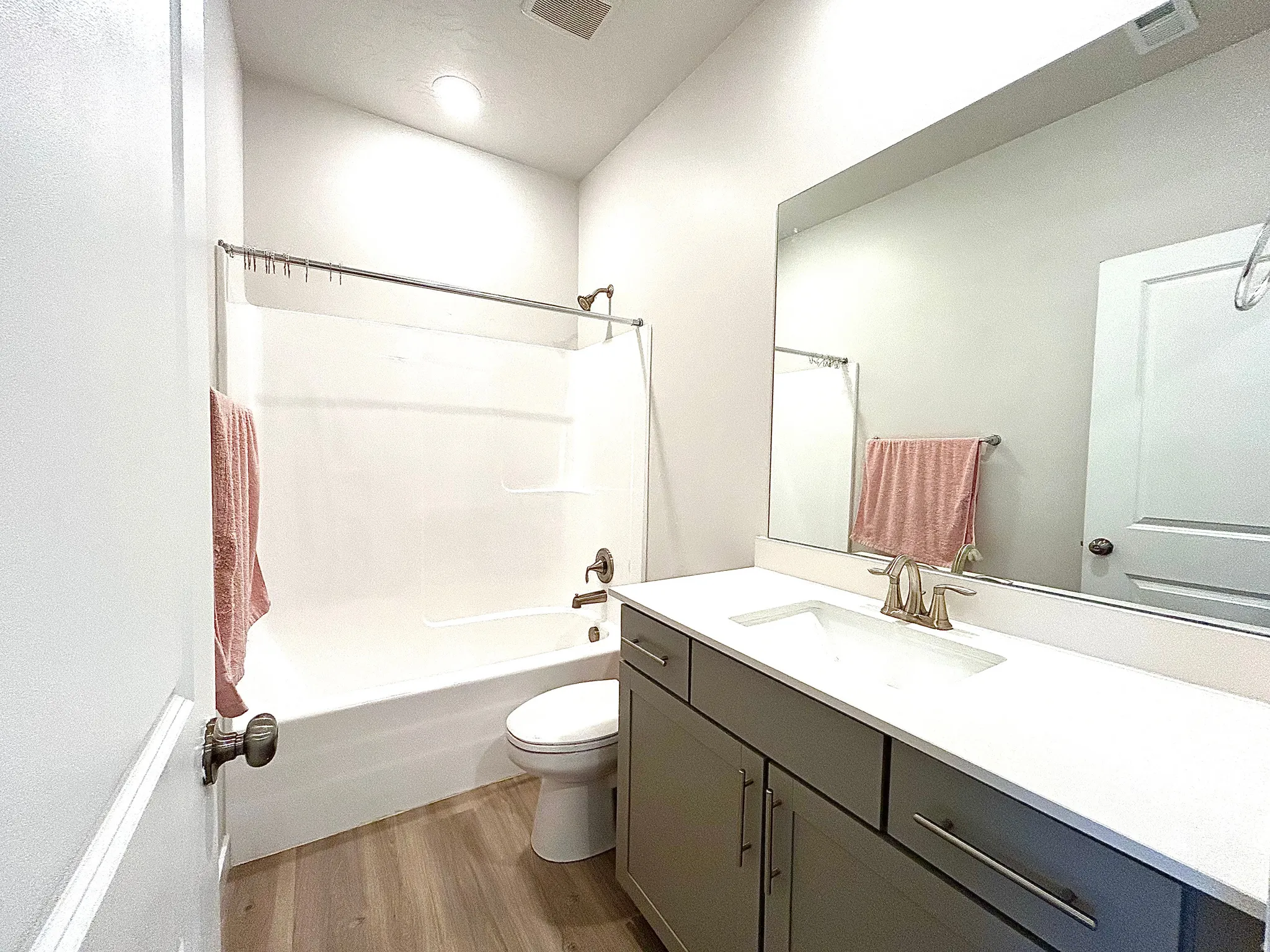 Bathroom featuring a vanity with a white countertop, an integrated rectangular sink, a large mirror, a white bathtub, and wood-finish flooring