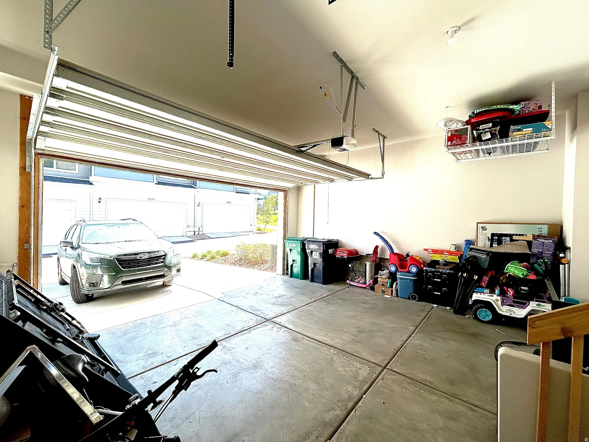 Concrete flooring, white walls, overhead garage door, built-in ceiling storage, and garage door opener